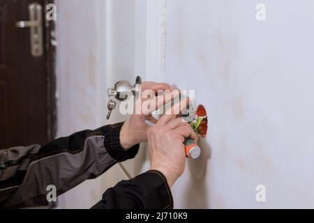 Hands of man electrician holding screwdriver working on the residential electric system installing power socket on wall Stock Photo