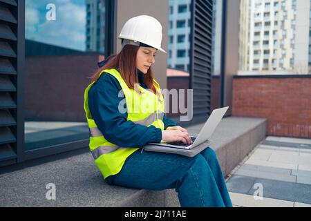 Female industrial engineers in hard hats discuss new project while using laptop at work on major construction site  Stock Photo
