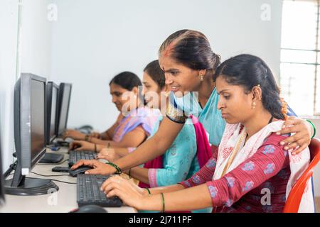 Teacher helping or teaching students during computer class training - concept of learning, personal support and technology. Stock Photo