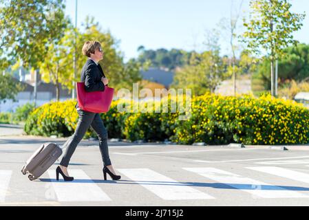 Traveling elegant businesswoman wearing sunglasses walking on crosswalk Stock Photo