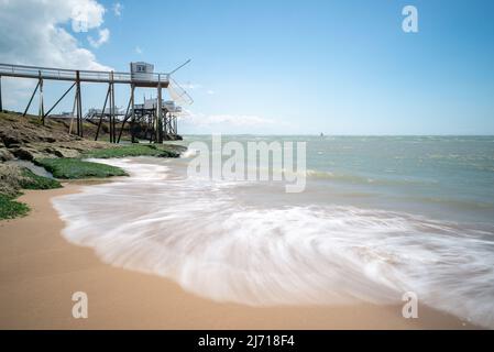 Ocean waves swashing on sandy beach at Charente Maritime on western Atlantic coast France with fishing huts on rocks in summer Stock Photo