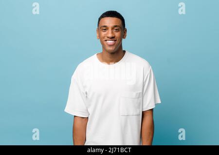 Portrait of cheerful young african-american guy wearing white casual t-shirt posing isolated on blue background. Carefree young millennial man looking at camera and laughing Stock Photo