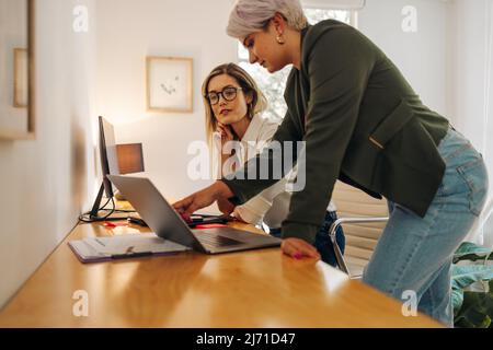 Female business partners having a discussion in a modern office. Two female entrepreneurs using a laptop while working as a team in a woman-owned comp Stock Photo