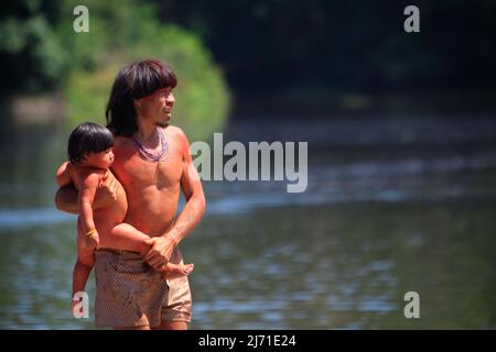 Indian father wearing tribal body paint holding baby by the Amazon river in Brazil, 2010. Stock Photo