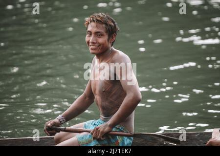 Indigenous caboclo man from an Amazon tribe in Brazil with tribal art painted on his body, riding canoe. Xingu River, Jogos Indígenas 2010. Stock Photo