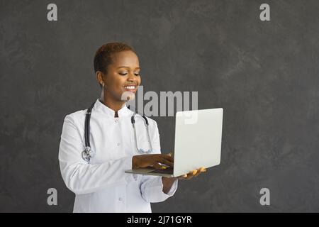 Happy smiling black female doctor using laptop computer isolated on grey background Stock Photo