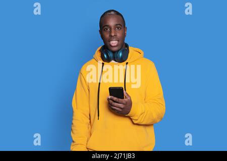 Cheerful African American man in yellow sweater using mobile phone application. Stock Photo
