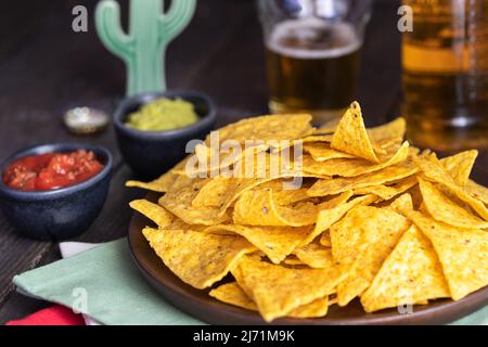Nachos with guacamole and red chilli sauces on wooden table. Mexican cuisine background Stock Photo
