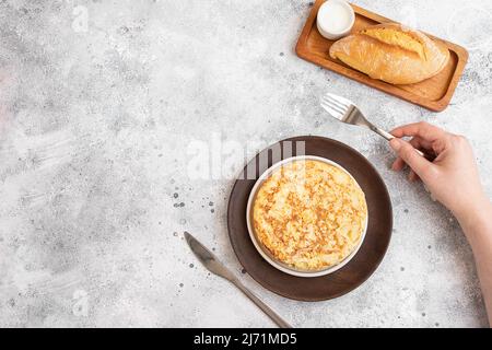Women hand holding fork ready to start eating Spanish omelette made with eggs and potatoes and served  with mayonnaise  and bread. Top view. Stock Photo