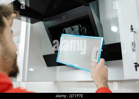 Mans hands removing a filter from cooker hood for cleaning or service. Replacing filter in kitchen hood. Modern kitchen fan or range hood. Stock Photo