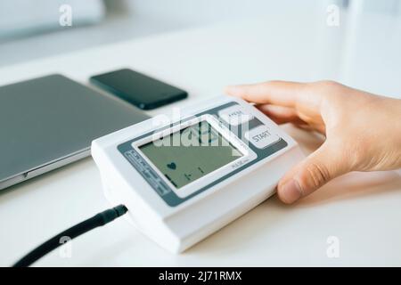Young man checking, measuring blood pressure with digital tonometer at home holding medical electronic device. Stock Photo
