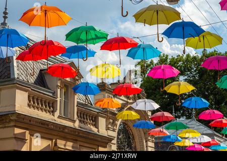 Lviv city colorful umbrellas on the street. Colored umbrellas hanging in the sky. Palace of arts. Street decorations. Multicolored umbrellas over blue Stock Photo