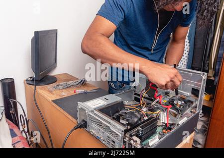 young brunette man with hair curlers at home cleaning and repairing desktop computer case, technical service and computing concept Stock Photo