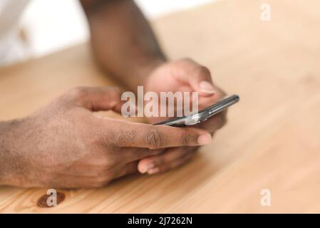 Hands of a black man browsing social networks or reading news on the phone at the table Stock Photo