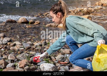 Woman on movement collecting trash as a voluteer in the river shore to clean up the enviroment Stock Photo