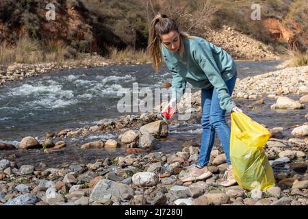 Save environment concept, young woman collecting garbage and plastic bottles on the river to dumped into the trash. Stock Photo