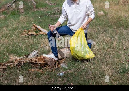 Unrecognizable man crouching down picking up bottle of alcohol after a music festival party Stock Photo