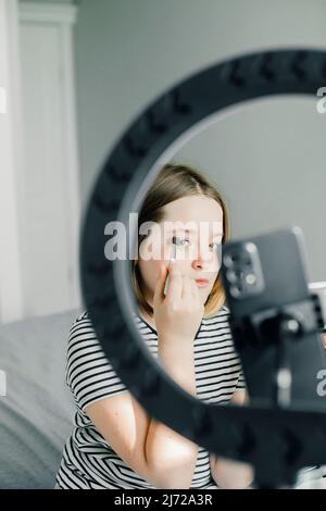 Teen girl beauty blogger with eyeshadows, brush and camera recording makeup tutorial video at home Stock Photo