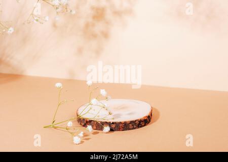 Wooden stand on pastel beige table with gypsophila flowers in sunlight. Mock up for perfume or cosmetic. Stock Photo