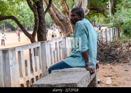 A sad Indian man is sitting on a bench in a park. He is looking down at ...