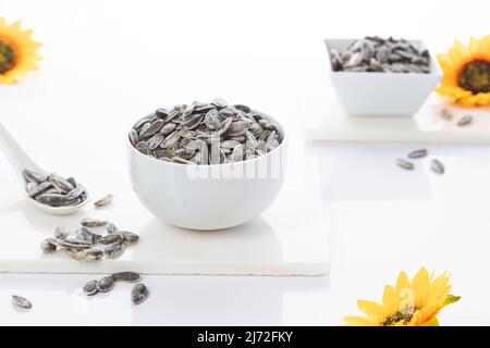Two bowls of sunflower seeds with sunflowers on white  background. Selective focus. Stock Photo