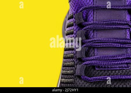 Lacing of purple black textile sneakers against yellow background. Laced fastening of new sport shoe close-up. Elastic laces of modern mesh sneakers. Stock Photo