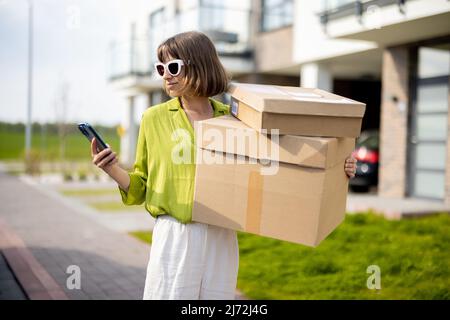 Woman using phone while standing with parcels on a street outdoors Stock Photo