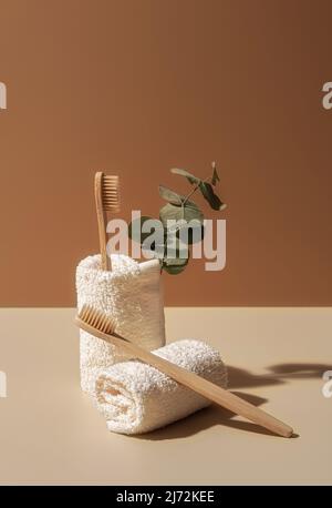 Organic wooden bamboo toothbrushes, towels and eucalyptus leaf on terracotta and beige background. Natural beauty and health concept. Eco-friendly zero waste design with copy space. Stock Photo