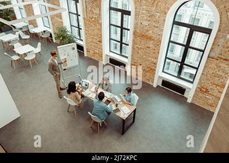 Male manager standing near the flipchart and talking with the team Stock Photo
