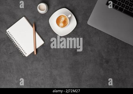 Workspace top view with laptop, notepad, pens and coffee on dark grey stone background. Flat lay with copy space. Business concept. Stock Photo