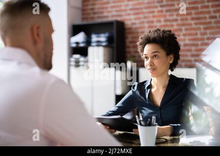 Mature Businesswoman Taking An Interview Of Man Over The Wooden Desk In Office Stock Photo
