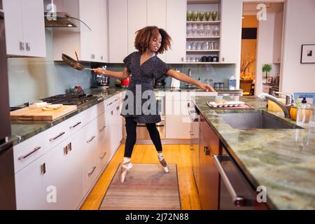 Ballet dancer standing on her toes and reaching for eggs while cooking in kitchen Stock Photo