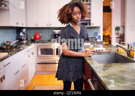 Young African American woman holding a spatula while cooking in a residential kitchen Stock Photo