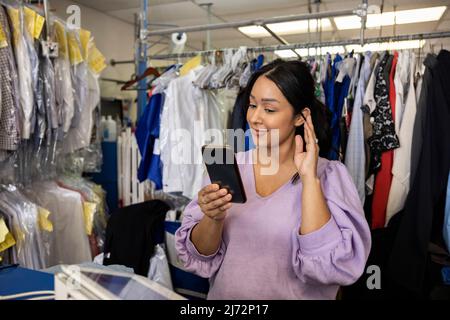 Hispanic woman talking on a facetime call while at working behind counter at a dry cleaners. Stock Photo