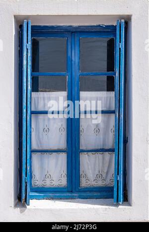 Window with pastel blue open wooden shutters on white wall. Cyclades island house front view, Greek traditional architecture. Stock Photo