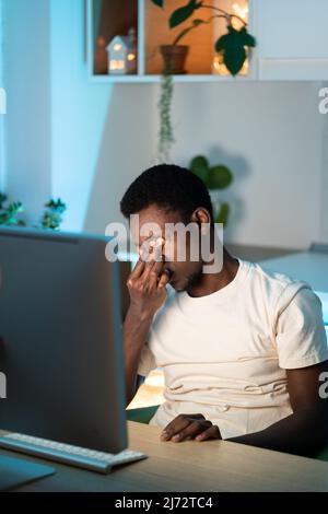 Tired freelance programmer man massage nose suffer from eyestrain working remote at computer at home Stock Photo