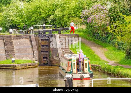 Canal narrowboat passing through locks on the Trent and Mersey canal as it passes through the village of Wheelock Cheshire England Stock Photo