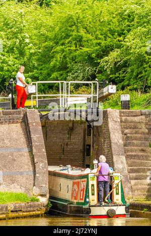 Canal narrowboat passing through locks on the Trent and Mersey canal as it passes through the village of Wheelock Cheshire England Stock Photo