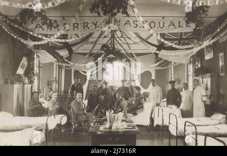 British army patients and medical orderlies in the military hospital based at Holmstone Camp, Lydd, Kent. The photograph was taken at Christmas 1916, during the First World War. The ward is decorated with paper chains, a handmade banner wishing visitors “A Merry Xmas To U All”, British Royal Navy White Ensign flags as well as other flags of the Allies, including the Japanese national flag. Stock Photo