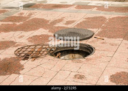 An open manhole on the road. Dangerous open unsecured hatch on the road. Accident with sewer hatch in city. Concept of sewage, repair of underground c Stock Photo