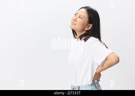 Osteochondrosis. Suffering from back pain after long study pretty young Asian woman touching painful lower back posing isolated on white background Stock Photo