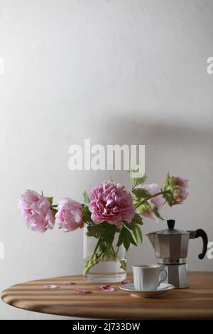 Cup of coffee, geyser coffee maker and bunch of peony flowers on wooden table. Copy space Stock Photo