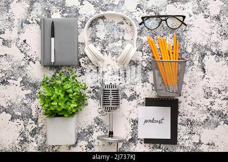 Microphone, headphones, paper with word PODCAST and eyeglasses on grunge background Stock Photo