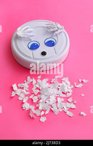 Modern robot vacuum cleaner with drawn eyes and paper pieces on pink background Stock Photo