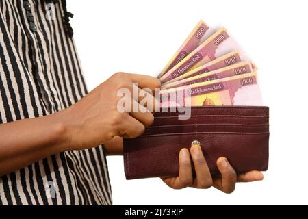 fair Female Hand Holding brown Purse With Afghan afghani notes, hand removing money out of purse isolated on white. removing money from wallet Stock Photo