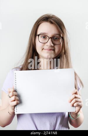 Teen girl wearing glasses showing blank sketchbook. Education
