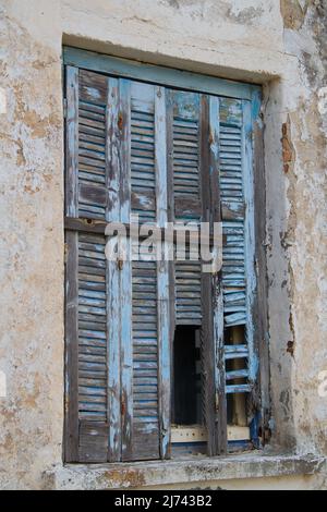 Pale blue weathered shutters on the window of a dilapidated building Stock Photo
