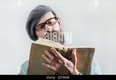 Portrait of serious bearded man in glasses and beret reading old book. Selective focus. Stock Photo