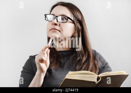 Thoughtful dreamy brunette woman in glasses reading a book. Female works on book review. Stock Photo