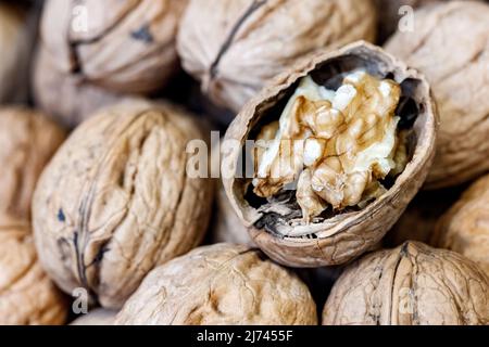 Closeup of split raw walnut on pile of whole walnuts with shells Stock Photo